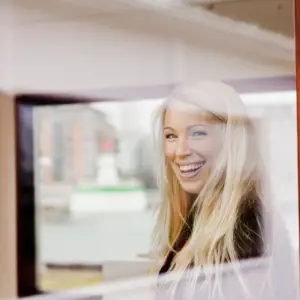 Kvinde smiler ud af vinduet forbi hun er glad for at bruge Microsoft 365 intranet