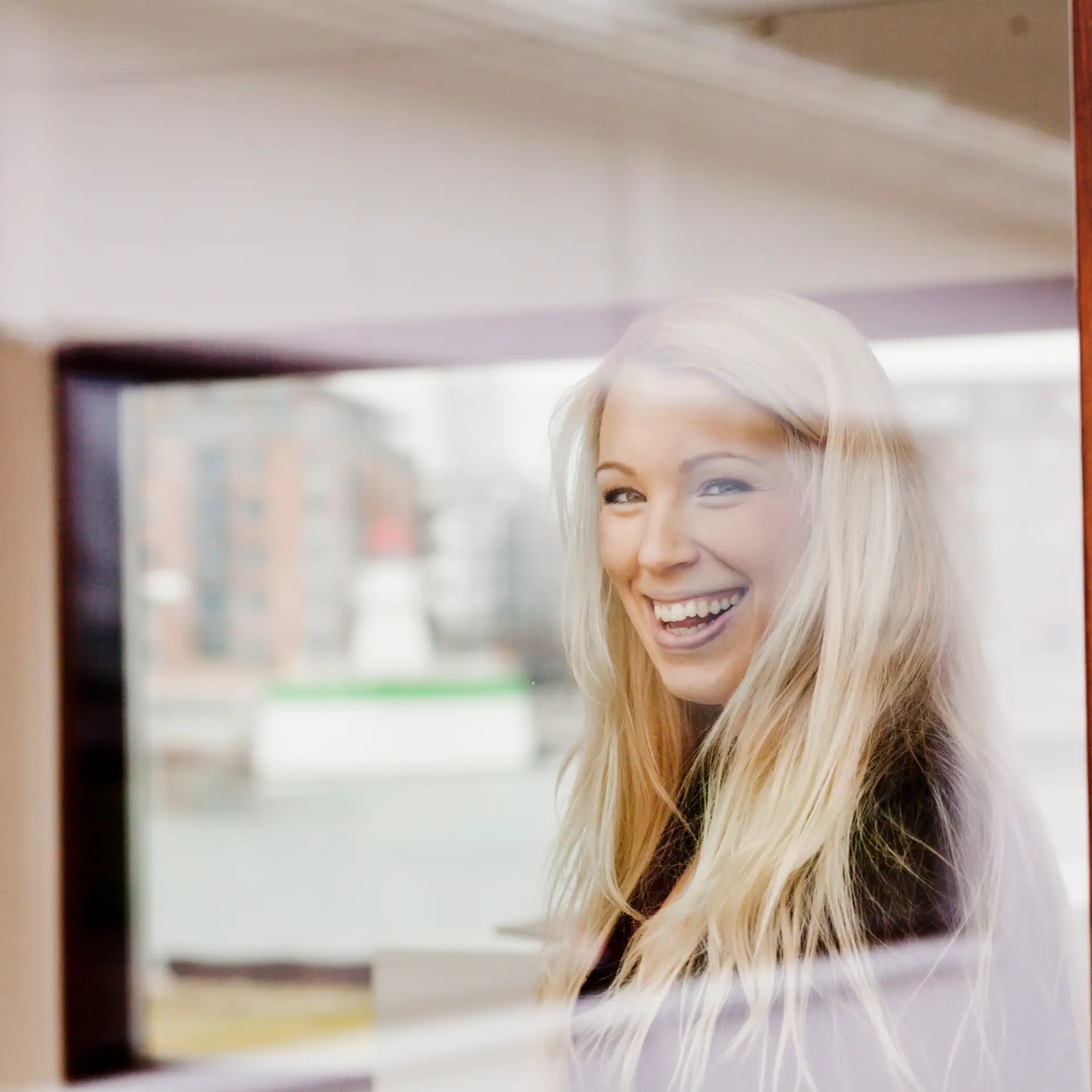 Kvinde smiler ud af vinduet forbi hun er glad for at bruge Microsoft 365 intranet
