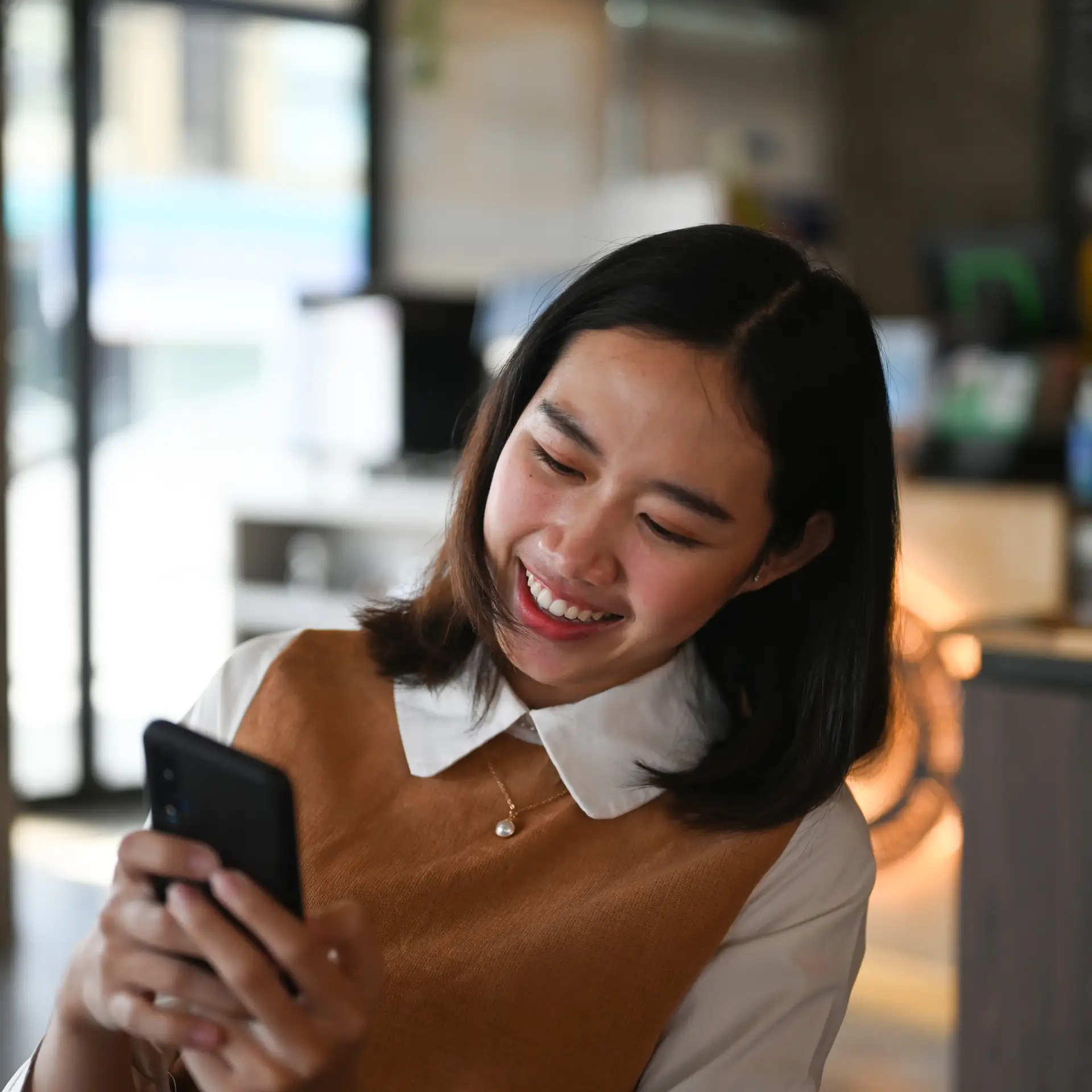 Kvinde smiler forbi hun bruger et godt intranet i SharePoint fra Blue Dock på sin telefon