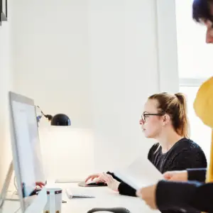 En kvindelig medarbejder sidder på et kontor og kigger på sin computer hvor hun er i gang med at optimerer sit online QMS på SharePoint, som er udarbejdet af Blue Dock