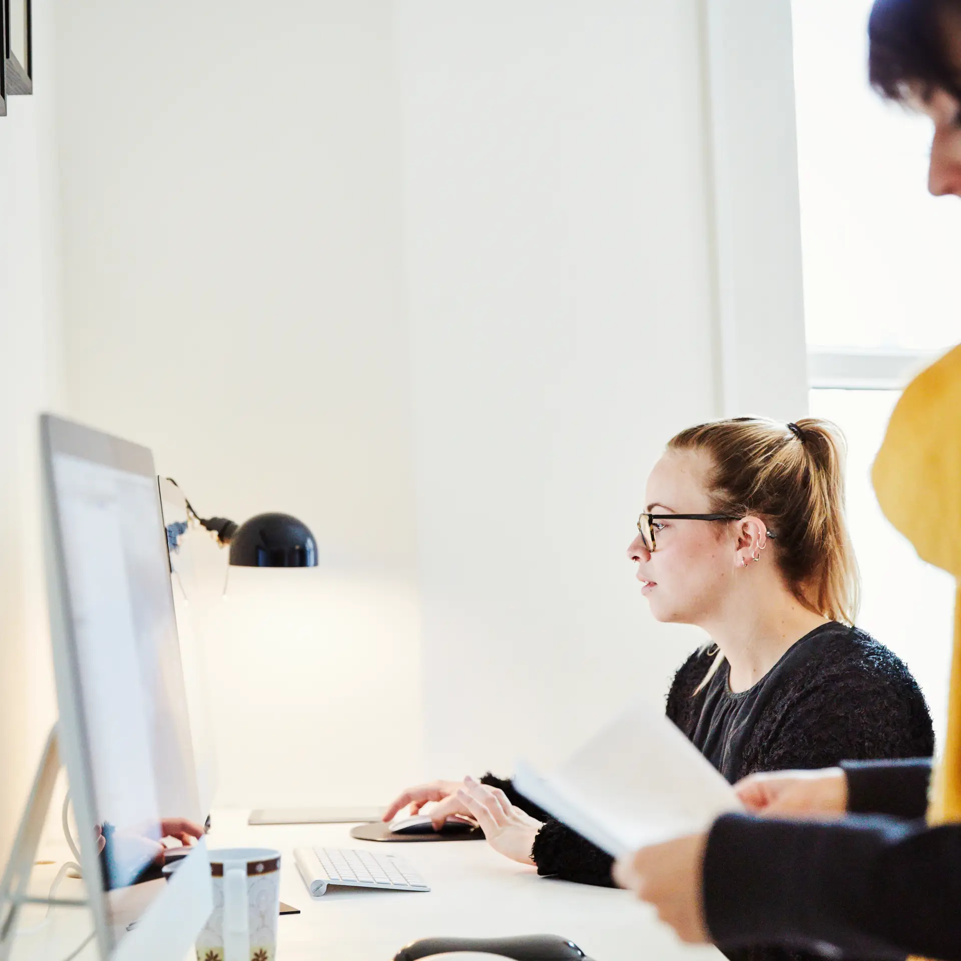 En kvindelig medarbejder sidder på et kontor og kigger på sin computer hvor hun er i gang med at optimerer sit online QMS på SharePoint, som er udarbejdet af Blue Dock